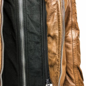 May include: A brown leather jacket with a black fleece lining. The jacket has a zipper closure and two zippered pockets.