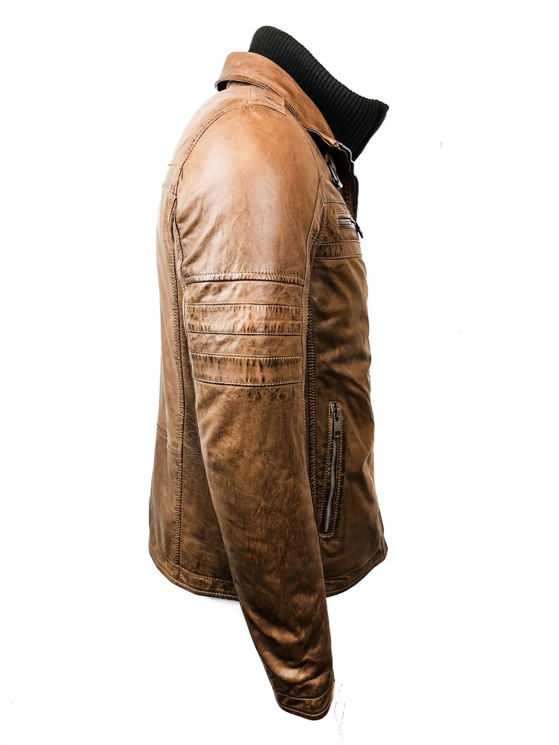 May include: A brown leather jacket with a zipper closure and a stand-up collar. The jacket has a zippered pocket on the left side and a decorative zipper on the right side.