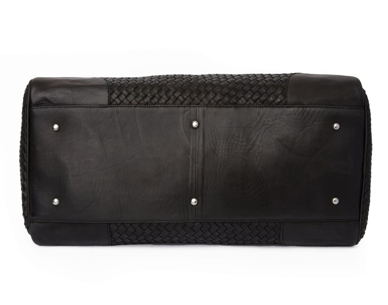May include: Black leather travel bag with a woven design. The bag has a rectangular shape and a zipper closure.