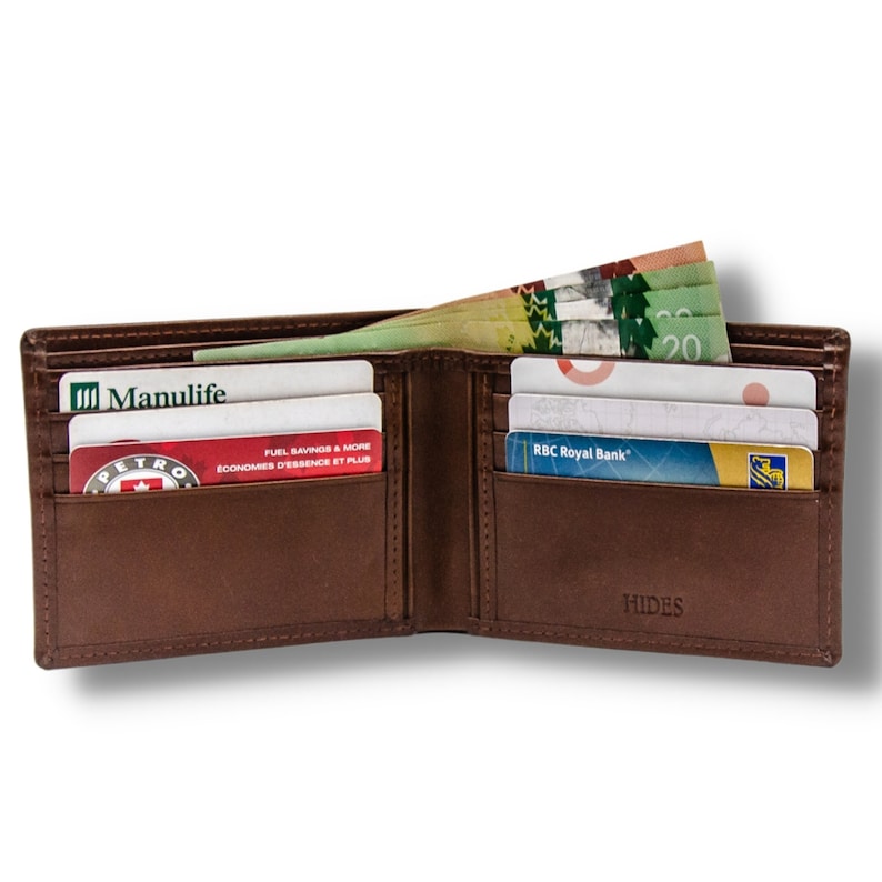 May include: A brown leather bi-fold wallet with multiple card slots and a money clip. The wallet is open and shows various cards including a Manulife card, a Petro-Canada card, and an RBC Royal Bank card. The wallet also has a HIDES logo on the outside.