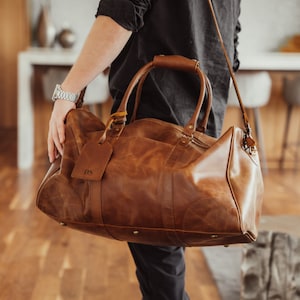 May include: A brown leather duffel bag with a long strap and a personalized leather tag that says "DS".