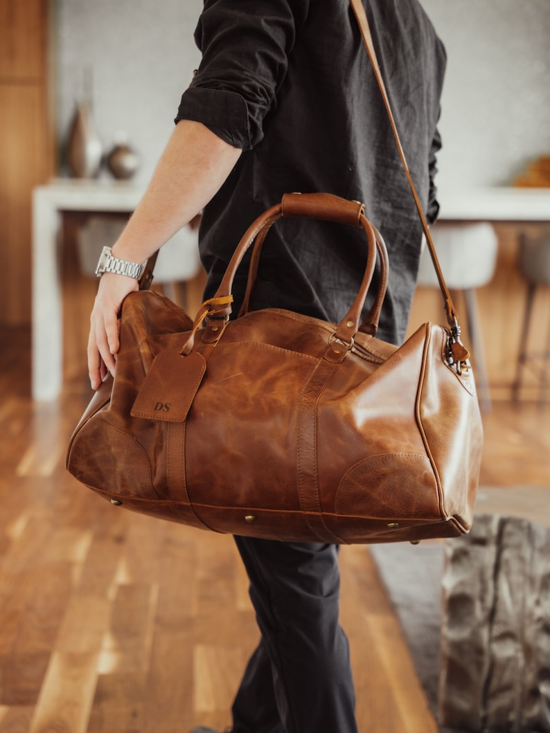 May include: A brown leather duffel bag with a long strap and a personalized leather tag that says "DS".