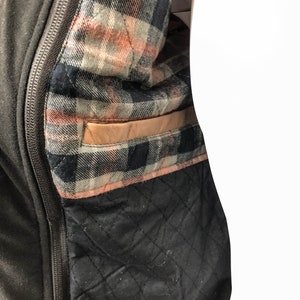 May include: A black jacket with a zipper closure and a plaid lining. The lining has a brown leather pocket.