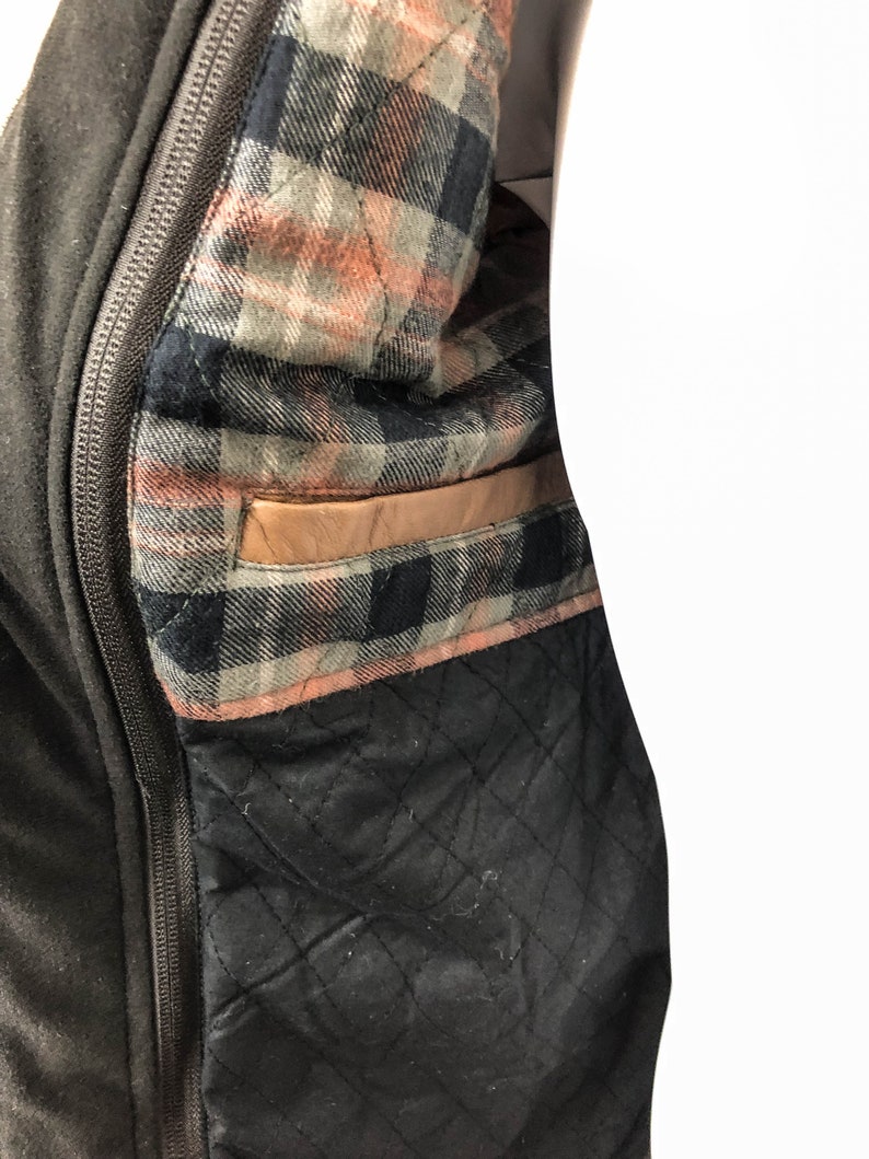 May include: A black jacket with a zipper closure and a plaid lining. The lining has a brown leather pocket.