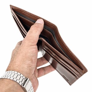 May include: A brown leather wallet is open and empty, held in a hand with a silver watch.