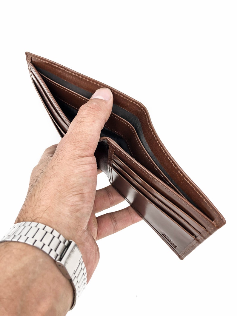 May include: A brown leather wallet is open and empty, held in a hand with a silver watch.