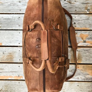 K&ouml;nnte beinhalten: Eine braune Ledertasche mit Rei&szlig;verschluss oben, zwei Griffen und einem verstellbaren Schultergurt. Die Tasche hat einen Used-Look und ist aus hochwertigem Leder gefertigt.