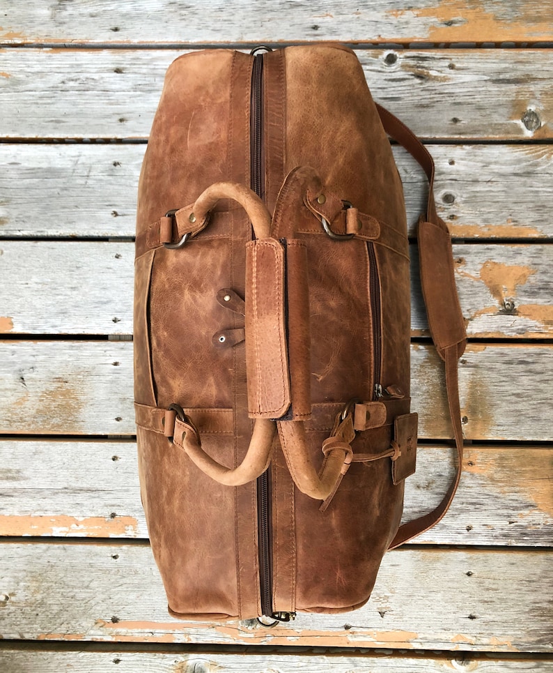 K&ouml;nnte beinhalten: Eine braune Ledertasche mit Rei&szlig;verschluss oben, zwei Griffen und einem verstellbaren Schultergurt. Die Tasche hat einen Used-Look und ist aus hochwertigem Leder gefertigt.