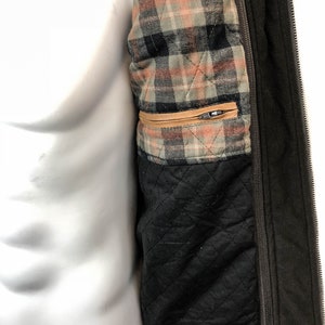 May include: A brown jacket with a zipper closure and a plaid lining. The lining has a brown, black, and white plaid pattern. The jacket has a brown leather trim.