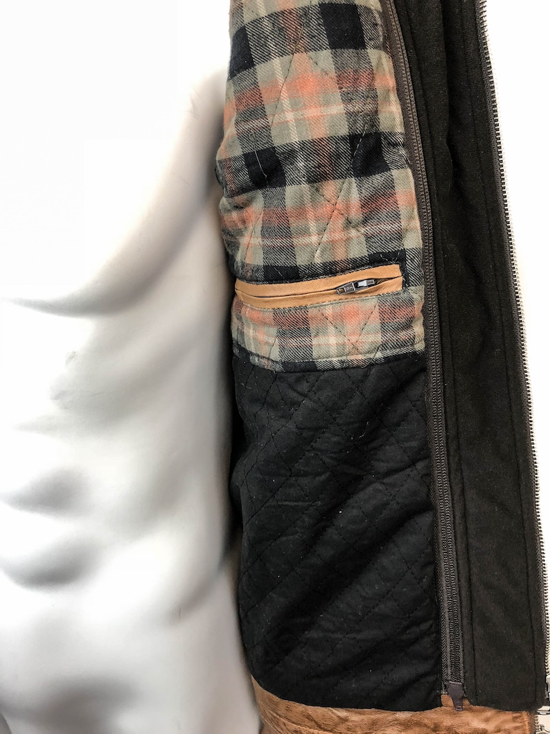 May include: A brown jacket with a zipper closure and a plaid lining. The lining has a brown, black, and white plaid pattern. The jacket has a brown leather trim.