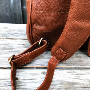 Pu&ograve; includere: Uno zaino in pelle marrone con spalline regolabili e fibbie in metallo dorato. Lo zaino &egrave; realizzato in pelle testurizzata e ha un design classico.