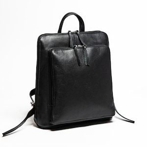 May include: A black leather backpack with a top handle and two zipped compartments. The backpack has a green zipper pull.