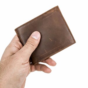 Pu&ograve; includere: Un portafoglio di pelle marrone tenuto in una mano.
