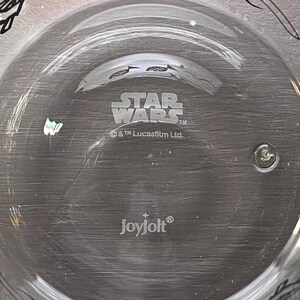 May include: Clear glass plate featuring the Star Wars logo and the Joyjolt brand name. The plate is circular with a raised edge. The Star Wars logo is in a bold, stylised font.