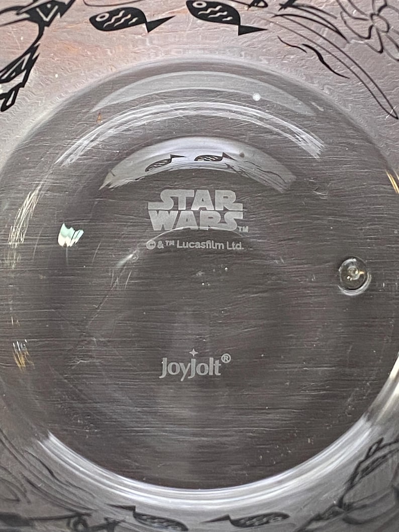 May include: Clear glass plate featuring the Star Wars logo and the Joyjolt brand name. The plate is circular with a raised edge. The Star Wars logo is in a bold, stylised font.