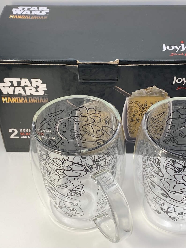 May include: Two double-walled glass mugs with handles, featuring a black and white Star Wars Mandalorian design. Each mug holds 400 ml. The mugs are displayed in front of a black box with the Star Wars Mandalorian logo.