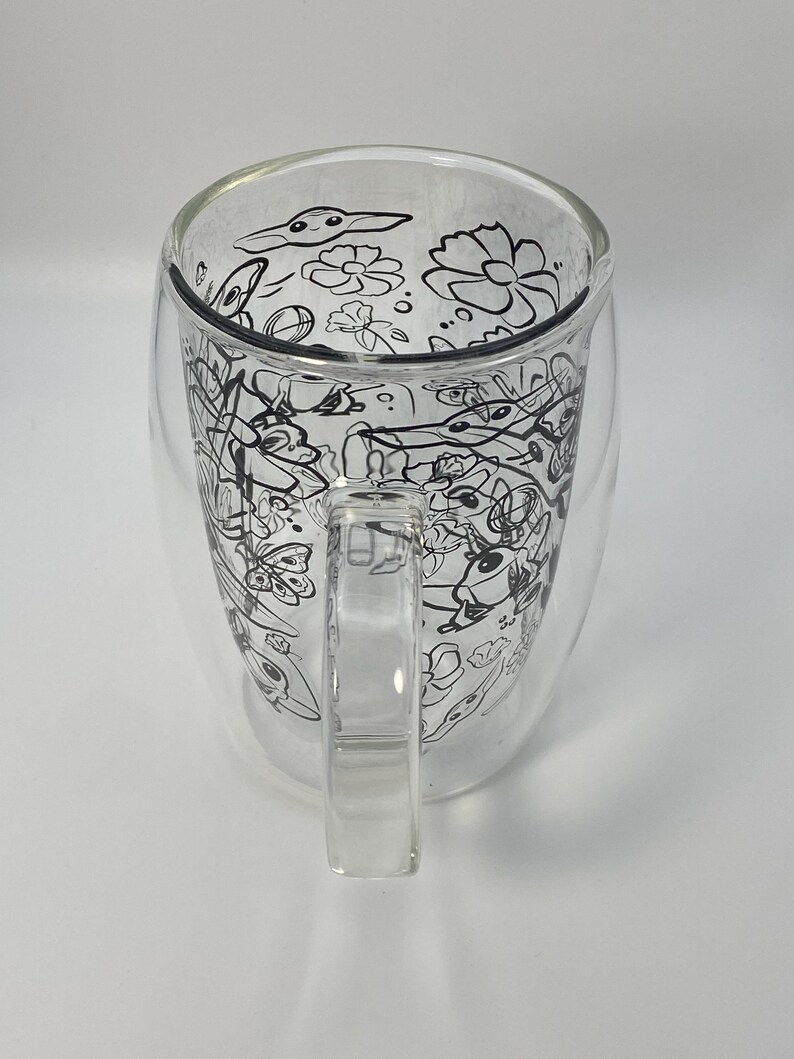 May include: A clear glass mug with a double-walled design. The interior features a black and white floral and abstract design. The mug has a clear handle and is suitable for hot or cold drinks.