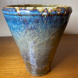 May include: A blue and brown ceramic vase with a wide mouth and a narrow base. The vase has a speckled glaze with a mottled effect.