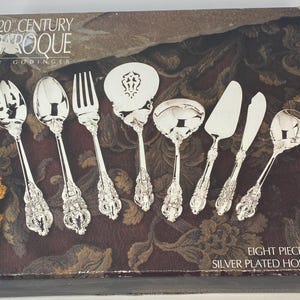 May include: A silver-plated eight-piece hostess set from the 20th Century Baroque collection by Godinger. The set includes serving spoons, a fork, a cake server, and knives, all with ornate handles. The box has a floral design.