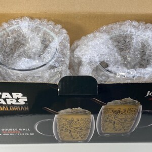May include: A boxed set of two double-wall glasses from Star Wars: The Mandalorian. Each glass has a capacity of 400 ml. The glasses have a decorative design. The box is black with the Star Wars logo and the JoyJolt brand name.