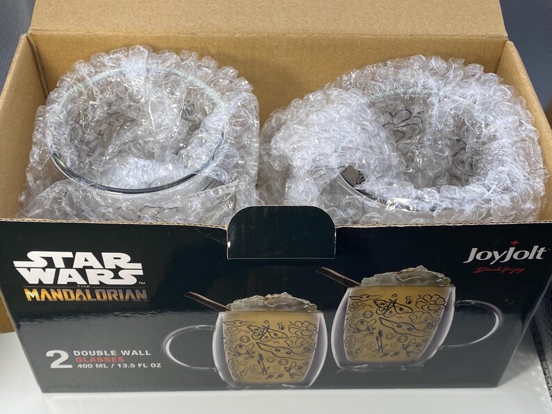 May include: A boxed set of two double-wall glasses from Star Wars: The Mandalorian. Each glass has a capacity of 400 ml. The glasses have a decorative design. The box is black with the Star Wars logo and the JoyJolt brand name.