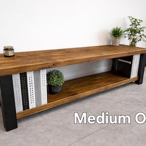 May include: A medium oak wooden bench with black metal legs. The bench has a lower shelf and decorative metal panels in black, white, and grey. Small potted plants and a candle sit on the bench. The text "Medium Oak" is visible.