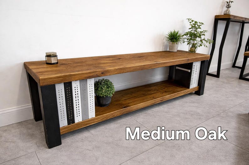 May include: A medium oak wooden bench with black metal legs. The bench has a lower shelf and decorative metal panels in black, white, and grey. Small potted plants and a candle sit on the bench. The text "Medium Oak" is visible.