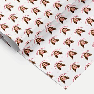 Op de afbeelding: Wit inpakpapier met een herhalend patroon van een vrouwen gezicht met de tekst "JASMINE IS 27!" in roze. De achtergrond heeft kleine roze stippen.