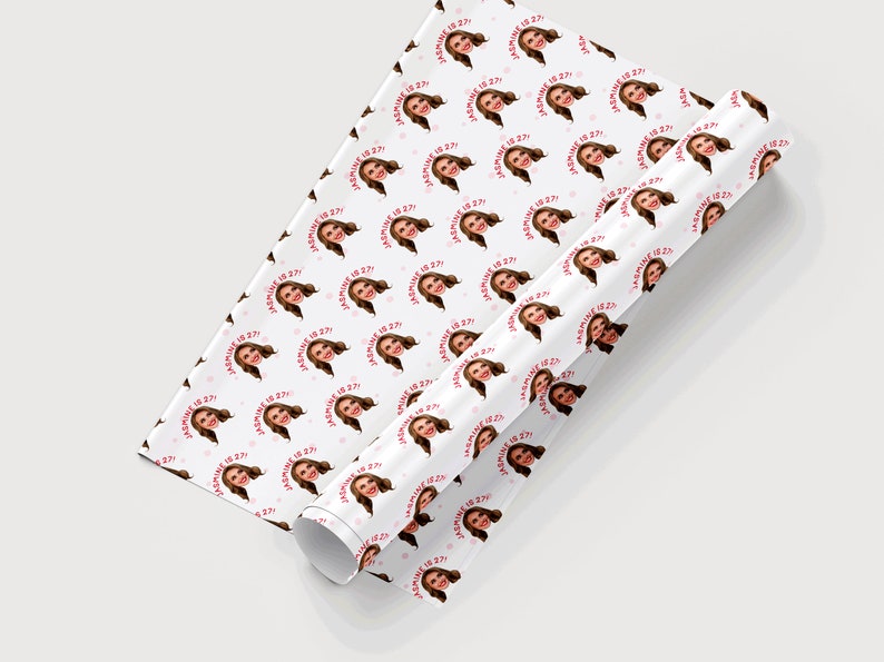Op de afbeelding: Wit cadeaupapier met een herhalend patroon van een vrouwen gezicht en de tekst "[Name] is 27!" in roze en rood.