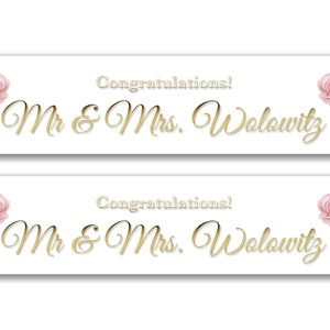 May include: Two white banners with pink floral designs and gold lettering. The text on the banners reads "Congratulations! Mr & Mrs Wolowitz".