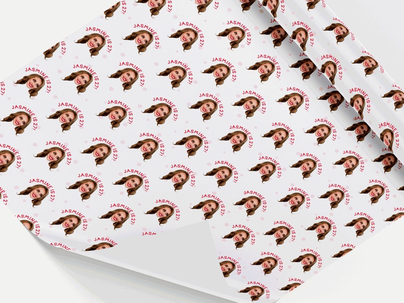 Op de afbeelding: Wit inpakpapier met een herhalend patroon van een vrouwengezicht in een cirkel met de tekst "JASMINE IS 27!" in roze. Er zijn kleine roze stippen verspreid over het papier.