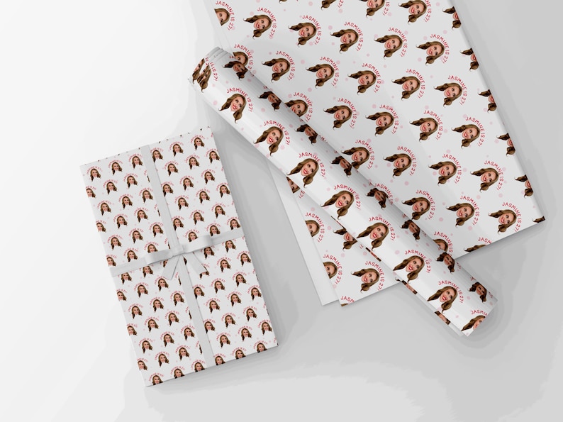 Op de afbeelding: Twee rollen wit inpakpapier met een herhalend patroon van een vrouwen gezicht en de tekst "Jasmine is 22!" in roze.