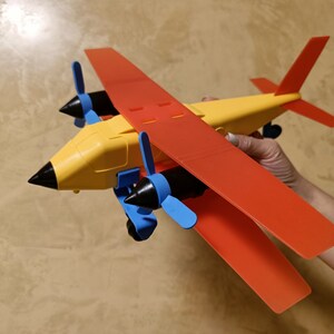 May include: A yellow and red toy airplane with two propellers. The propellers are black with blue blades. The airplane has a pointed nose and a tail.