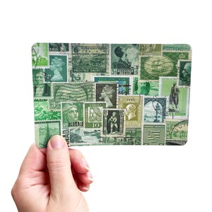 May include: A rectangular card filled with green postage stamps, held in a hand. The stamps depict portraits, ships, and other designs. The card has rounded edges. The background is white.
