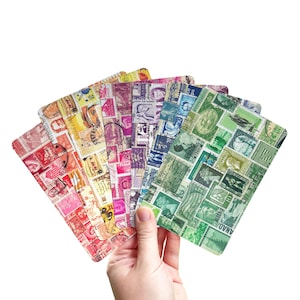 May include: A hand holds a fanned collection of rectangular cards, each covered with a collage of vintage postage stamps. The cards display a variety of colors, including red, yellow, purple, blue, and green, showcasing a diverse range of designs and historical imagery.