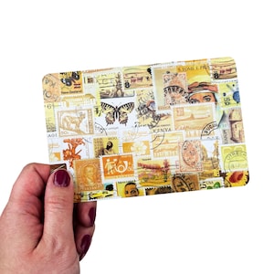 May include: A rectangular postcard with a yellow hue, covered in a collage of vintage postage stamps. The stamps display diverse designs, including butterflies, portraits, and international landmarks. The postcard is held by a hand.
