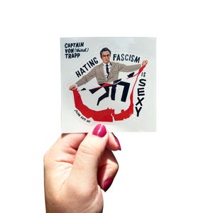 Könnte beinhalten: Ein Aufkleber mit einer Illustration im Vintage-Stil eines Mannes im Anzug, der ein rotes Banner mit den Worten "Hating Fascism is Sexy" hält. Der Aufkleber enthält auch den Text "Captain Von (thirst) Trapp" und "Julian Kate Art".
