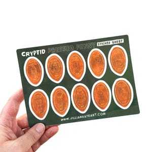 May include: A sticker sheet with Cryptid Pressed Penny designs. The sheet has a dark green background with eleven penny-shaped stickers. Each sticker has a copper-coloured design of a cryptid creature and the state abbreviation. The text "CRYPTID PRESSED PENNY STICKER SHEET" is at the top.