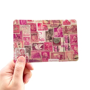 May include: A rectangular pink and white collage of vintage postage stamps. The stamps feature portraits, buildings, and text from various countries. The collage is held in a hand against a white background.