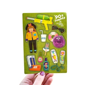 Puede incluir: Una hoja de pegatinas verde con un tema de verano de los 90, con ilustraciones de una pistola de agua, gafas de sol, un CD, una mochila, una muñeca, una bebida, un helado de conejo, un buscapersonas, un teléfono, una cinta de cassette y una botella. El texto "90s Summer" es visible.