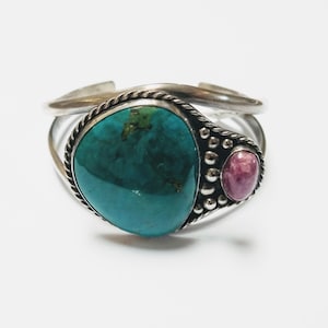 May include: A silver bracelet with a large turquoise stone and a smaller pink stone. The bracelet is decorated with small beads.