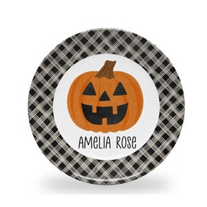 May include: A black and white checkered plate with a cartoon jack-o'-lantern and the name "Amelia Rose" printed on it.