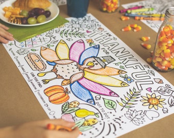 May include: A Thanksgiving-themed coloring placemat with a turkey illustration, the words "I am thankful for" and "Dot to Dot". The turkey is colored with various colors. A person is coloring with an orange crayon.