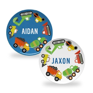 May include: Two blue and white round plates with a circle of construction vehicles around the edge. The blue plate has the name "AIDAN" in the center and the white plate has the name "JAXON" in the center.