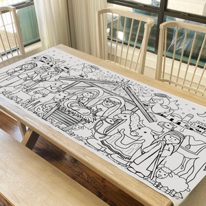 May include: A white, rectangular table runner featuring a black and white illustration of a nativity scene. The design includes figures of Mary, Joseph, baby Jesus, angels, animals, and the three wise men. The runner is placed on a wooden table.