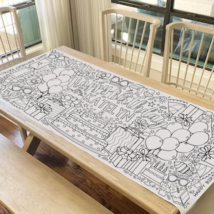 May include: A black and white coloring table runner with the words "Happy Birthday Katelyn" and various birthday-themed illustrations, including balloons, presents, cake, and stars.