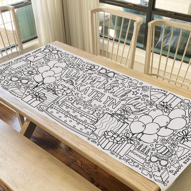 May include: A black and white coloring table runner with the words "Happy Birthday Katelyn" and various birthday-themed illustrations, including balloons, presents, cake, and stars.