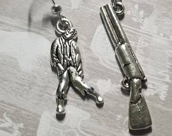 May include: Silver-toned metal earrings. One earring features a zombie figure, the other a shotgun. The earrings have a hook closure. The zombie figure is in a walking pose. The shotgun has a detailed design.