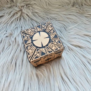 May include: A black and gold metal puzzle box with a circular design on the top. The box is made of many interlocking pieces.