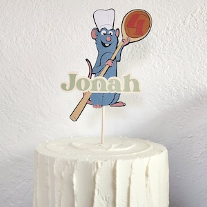 May include: A white frosted cake with a decorative topper featuring a cartoon rat chef holding a wooden spoon. The spoon has a number 4 on it. The name "Jonah" is printed in green letters below the rat.